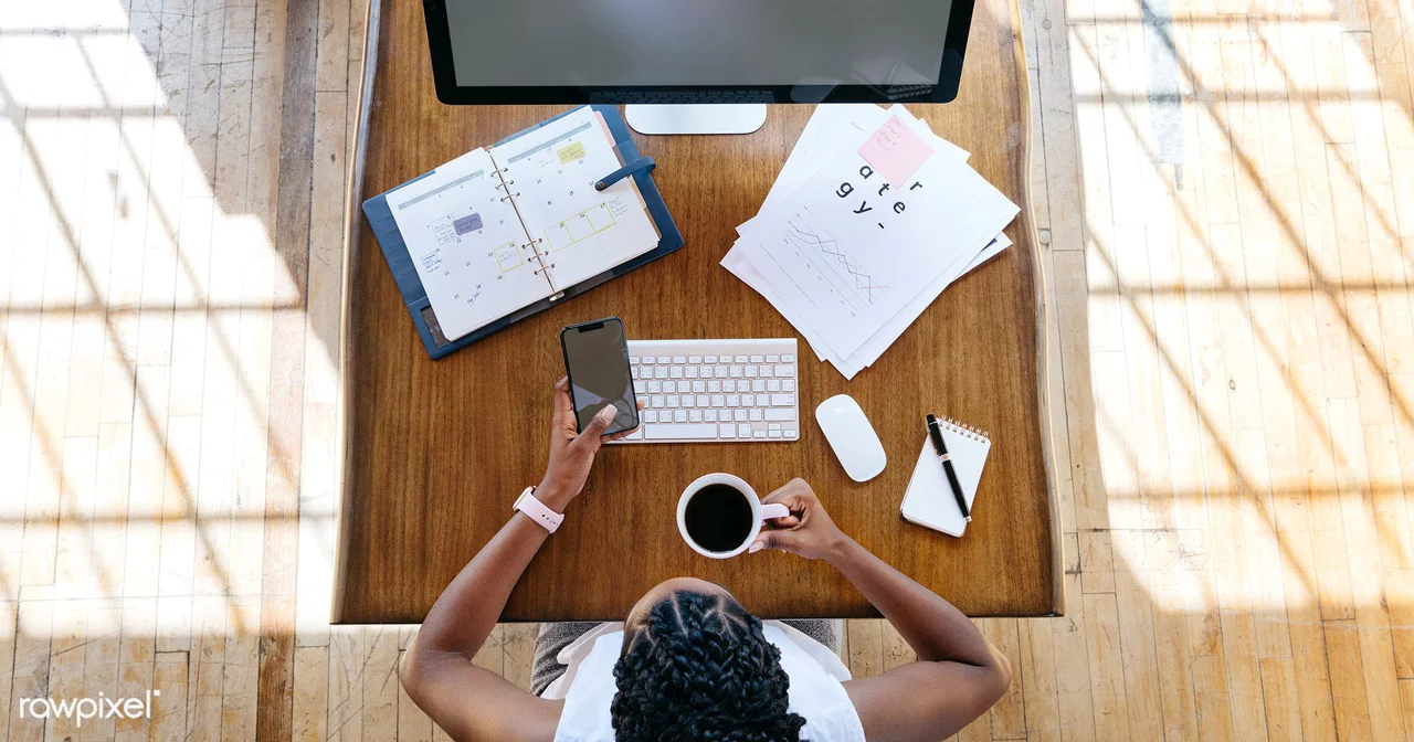 Designer mulher negra tomando café em em sua mesa de trabalho em frente a macbook