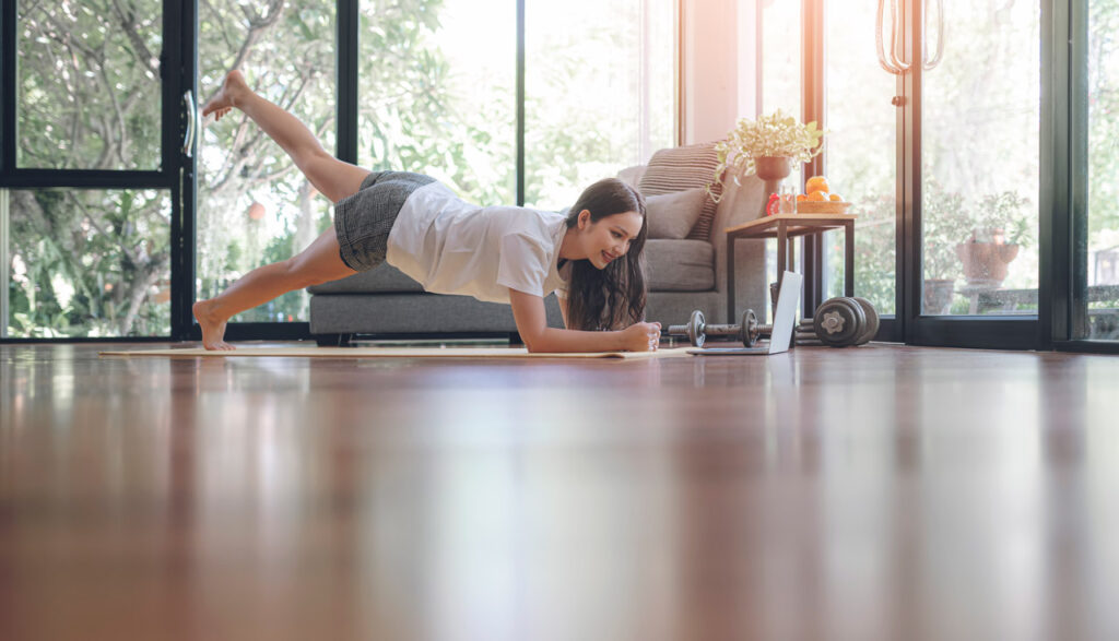 Mulher jovem praticando Pilates em casa na posição prancha com elevação de uma perna