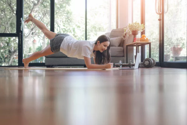 Mulher jovem praticando Pilates em casa na posição prancha com elevação de uma perna