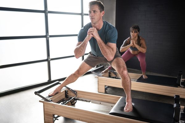 Homem e mulher em um aparelho reformer de pilates